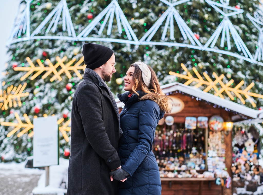 happy-couple-wearing-warm-clothes-hold-hands-and-look-at-each-other-standing-near-a-city-christmas-tree-enjoying-spending-time-together.jpg